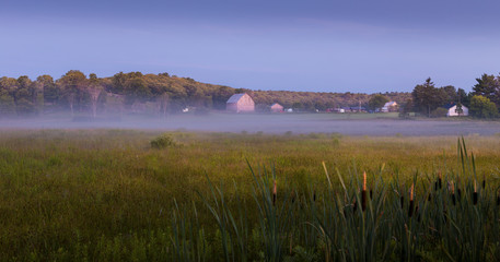 Farm with a wood barn and houses next to a grass field at sunrise. © Adam