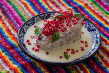 Chile en nogada en plato de talavera poblana en fondo colorido o reboso de colores mexicanos