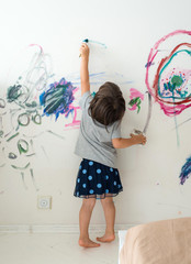 Curly cute little toddler girl painting with paints color and brush on the wall. Works of child