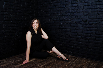 Portrait of a beautiful brunette girl in black jumpsuit sitting and posing in the studio.