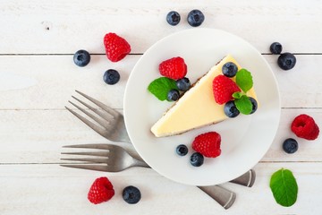 Slice of cheesecake with blueberries and raspberries, top view scene over a bright, white wood background