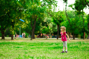 Little girl play with flying disk in motion, playing leisure activity games in summer park