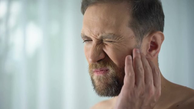 Male suffering from tooth ache, touching cheek, pulp inflammation, gingivitis