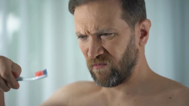 Caucasian man brushing teeth and seeing blood on toothbrush, dental care, ache