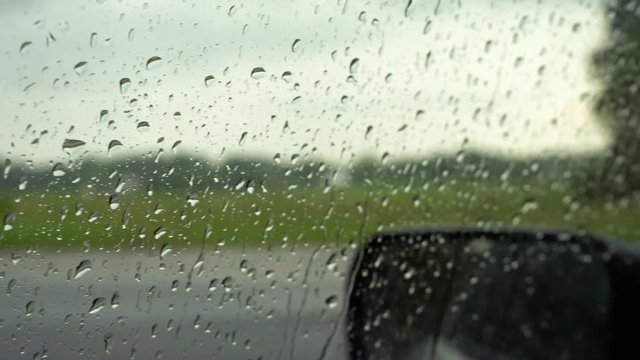 Pan to the right of water droplets on a car window while raining 4K.