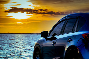 Blue compact SUV car with sport and modern design parked on concrete road by the sea at sunset....