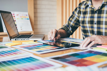 Fototapeta premium Creative graphic designer using graphics tablet to choosing color swatch samples chart for selection coloring with work tools and accessories while working with computer at studio