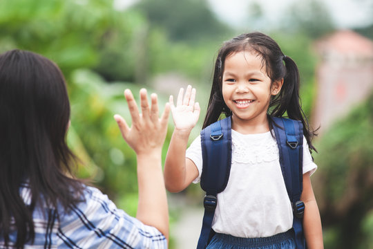 Back to school. Cute asian child girl with school bag and her mother making hi five gesture before go to school with fun