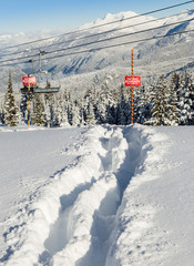 Tracks in the snow beside a ski area boundary sign.