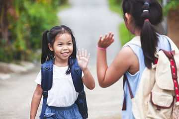 Back to school. Cute asian child girl with school bag and her elder sister making hi five gesture...