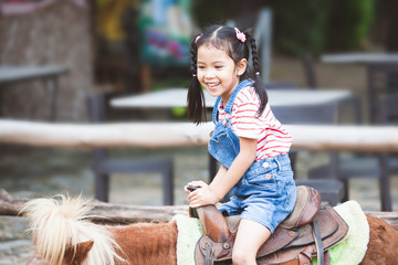 Cute asian child girl riding a pony in the farm with fun