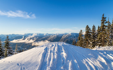 Ski tracks dropping off a ridge, looking out onto the mountains near Whistler, BC.