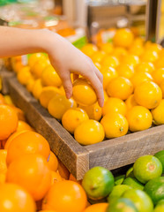 A hand picking up a lemon in the produce section of a grocery store.