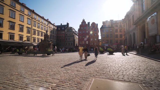 People walking on Stortorget in the Old Town of Stockholm Sweden. Steady glide cam footage moving backwards. Beautiful old Swedish architecture in Gamla Stan. A sunny summer day in July.