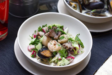 Warm salad with seafood mussels, octopus and fresh vegetables in deep plate on the table