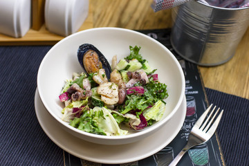 Warm salad with seafood mussels, octopus and fresh vegetables in deep plate on the table