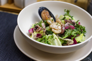 Warm salad with seafood mussels, octopus and fresh vegetables in deep plate on the table