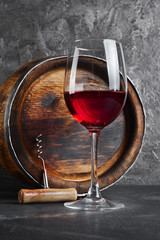 Glass with red wine for tasting and wooden barrel in dark cellar