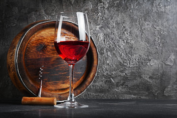 Glass with red wine for tasting and wooden barrel in dark cellar