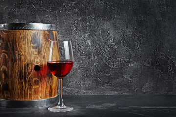 Glass with red wine for tasting and wooden barrel in dark cellar