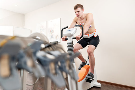 A male patient, pedaling on a bicycle ergometer stress test system for the function of his heart checked. Athlete does a cardiac stress test in a medical study, monitored by the doctor.