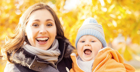 Mother playing in park with her toddler baby. Mom and son over seasonal autumn background.