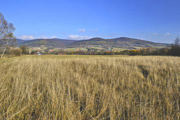  Field with dried yellow grass, hills and houses under  blue sky on a warm autumn  day. Countryside landscape in Low Beskids (Beskid Niski), Poland