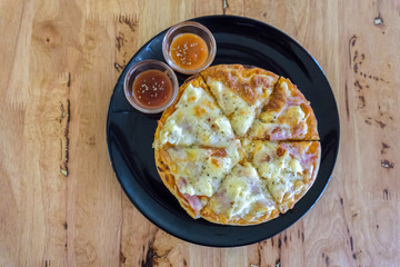 Bacon and cheese pizza served in black plate on the wooden table
