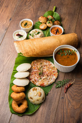 Group of South Indian food like Masala Dosa, Uttapam, Idli/idly, Wada/vada, sambar, appam, semolina halwa, upma served over banana leaf with colourful chutneys, selective focus