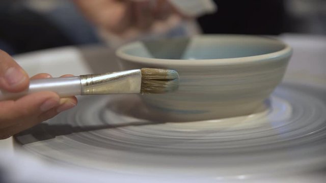 Close up of brush painting bowl on pottery wheel