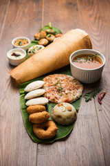 Group of South Indian food like Masala Dosa, Uttapam, Idli/idly, Wada/vada, sambar, appam, semolina halwa, upma served over banana leaf with colourful chutneys, selective focus