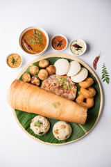 Group of South Indian food like Masala Dosa, Uttapam, Idli/idly, Wada/vada, sambar, appam, semolina halwa, upma served over banana leaf with colourful chutneys, selective focus