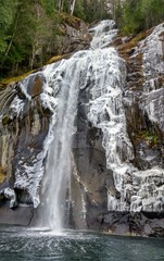 A waterfall by the ocean in winter, partially frozen on cliff rocks