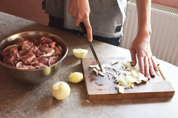 Man cutting onions on brown wooden chopping board for pork meat marinade.