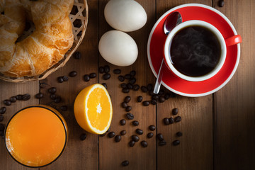 still life of breakfast set of croissants, fresh orange juice, eggs and hot black coffee on wooden table