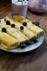 Pancake rolls, roast without fat, wraped with white cheese. They were sprinkled with blueberries. Blueberry cocktail with fresh blueberries
