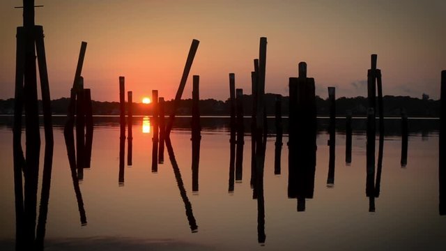 Beautiful sunrise over still water reflecting scattered pilings from an old pier.
