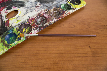 A palette full of old paint and a paintbrush on a wood table