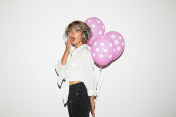 Surprised girl in white shirt amazedly looking in camera with pink balloons in hand over white background isolated