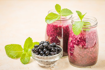Blueberry smoothie decorated with fresh green mint leaves and raw ripe berries on yellow pastel background.