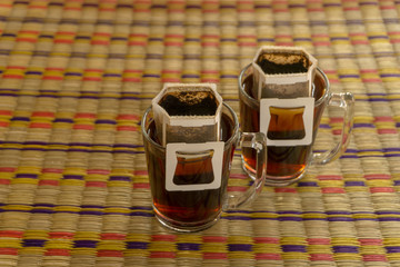 Two drip fresh coffee sachets on the transparent glass coffee cup with dripped coffee inside. They...