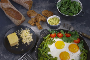 Fried eggs in an old pan with tomatoes, avocado pesto, green beans, pepper and salad on a dark background