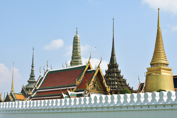 Naklejka premium View of Wat Phra Kaew (Temple of the Emerald Buddha) behind white wall, beautiful yellow pagoda brighting and bright sky in background