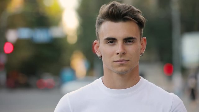 Closeup portrait of young handsome man looking smiling at camera, urban background