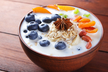 Oatmeal porridge with milk, fruits and peanuts on wooden background, healthy porridge with banana and peach slices, breakfast with fiber, anise, dried apricots in milk