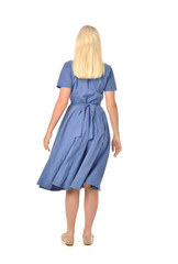 full length portrait of blonde girl wearing blue dress. standing pose with back to the camera. isolated on white  studio background.