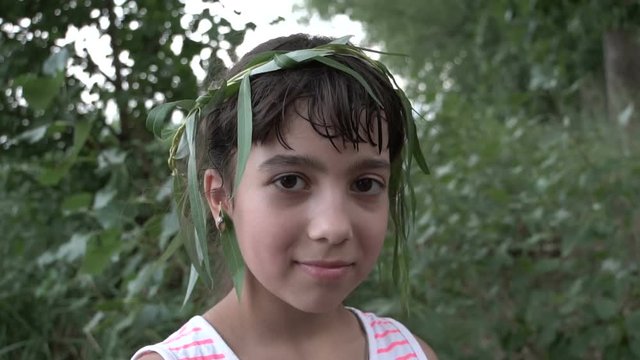 The girl looks at the camera. The leaves on the head. Serious kind. Dark hair. Eastern type. Children's holiday. Close-up portrait. Summer time.