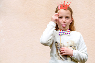 Funny little girl  with crown red paper mask showing tongue at kids birthday, Hallowen, Purim / fool day party.Copy space.Suitable for greeting card, invitation, poster, proposing product.