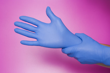 Hands wearing a blue latex glove, isolated on pink background