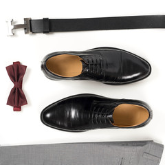 Close up of modern man accessories. Bordeaux bow tie, leather shoes, belt on white  background. Set for formal style of wearing isolated on white background. Top view.